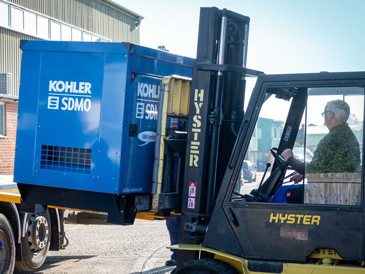 Kohler-SDMO generator being loaded by forklift on to the back of a flatbed trailer ready for transportation. Residential generator install